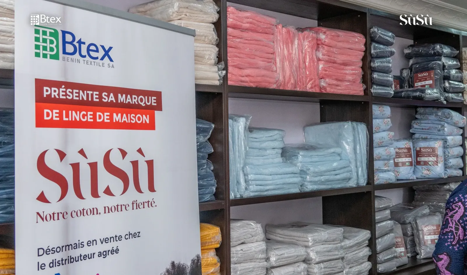 Shelves of Sùsù sheets and towels in the store, next to a Bénin Textile poster